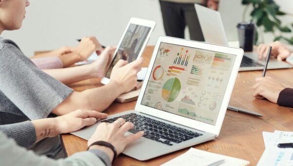 Aplikasi Keuangan Terbaik untuk Mengatur Uang ditampilkan pada ilustrasi seseorang mencatat keuangan di meja kerja dengan laptop dan dokumen anggaran