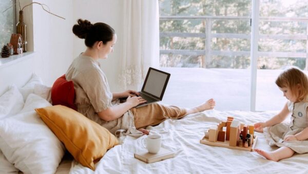 Ibu rumah tangga bekerja dari rumah menggunakan laptop sambil mengawasi anak bermain, contoh ide usaha ibu rumah tangga dari rumah